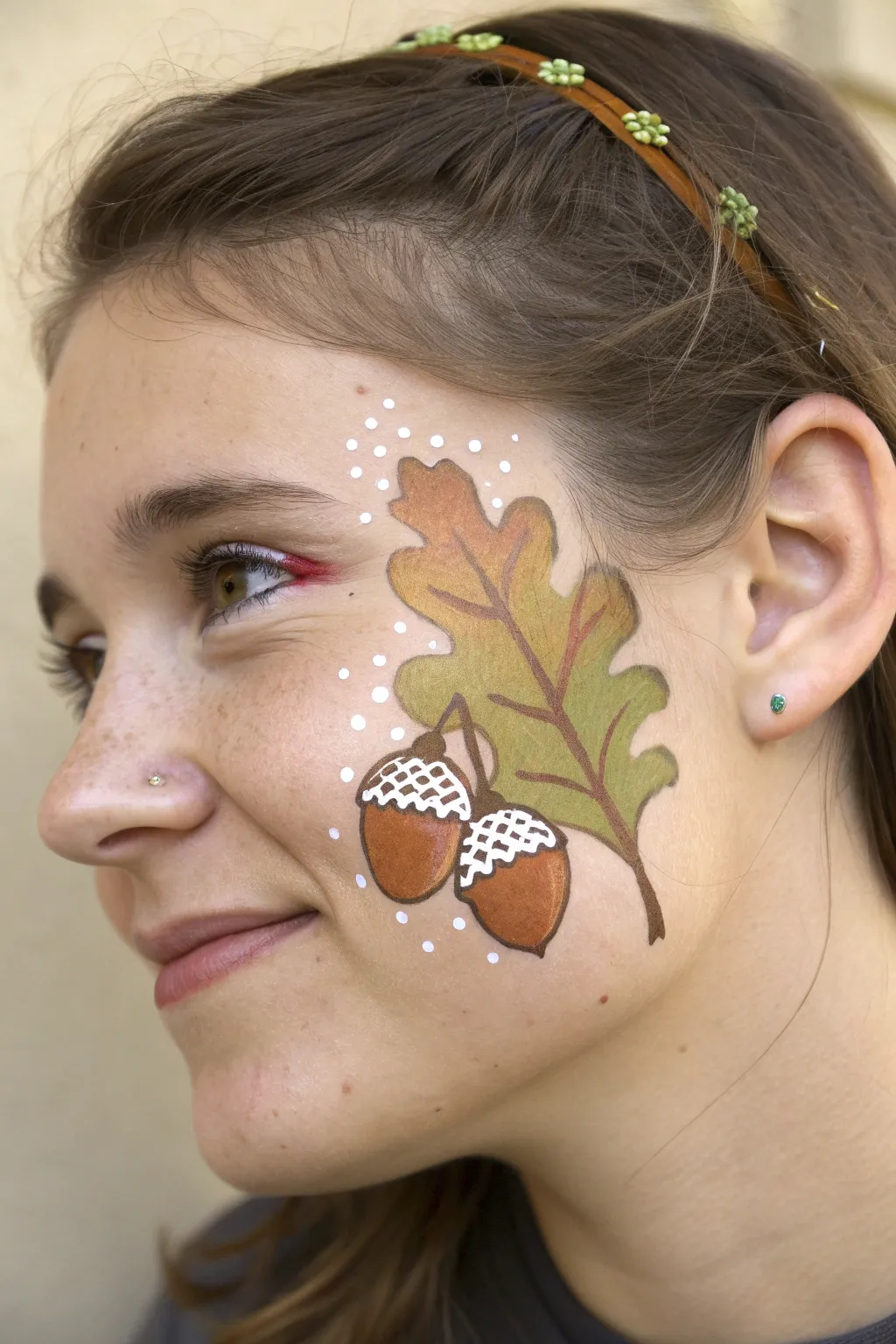 Warm acorn and oak leaf cheek cluster with glossy highlights for minimalist fall festival face paint