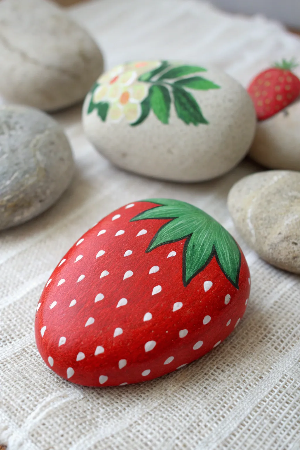 Sweet strawberry rock paint idea: one finished berry and one half-painted for easy DIY inspiration