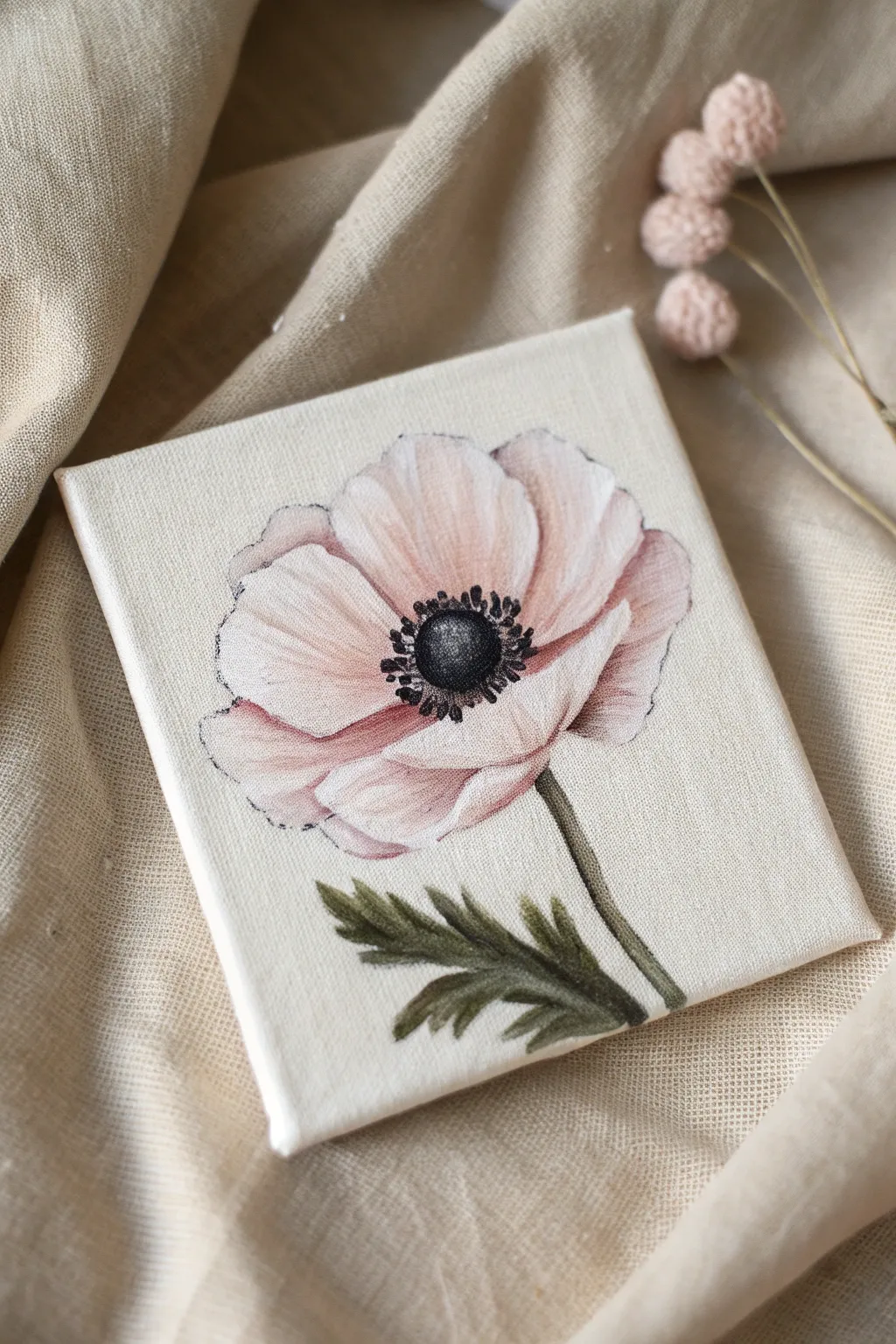 Paint a tiny anemone portrait: pale petals, bold dark center, simple stem on mini canvas.