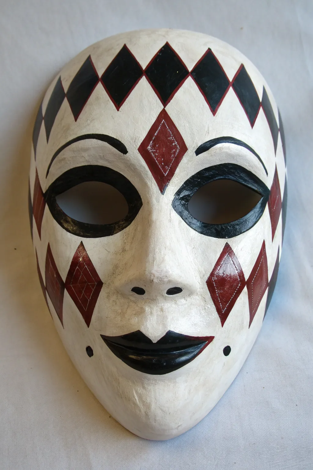 Minimalist white jester mask with crisp harlequin diamonds, bold red and black contrast