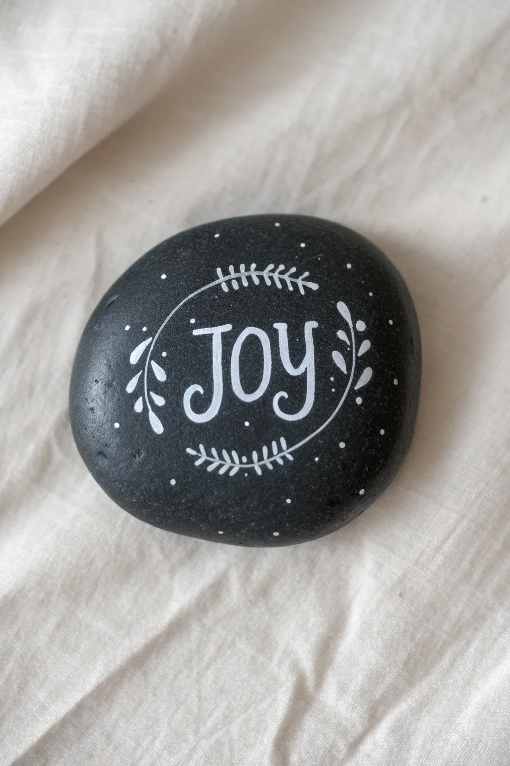 Minimalist black rock with bright hand-lettered Joy and delicate snowy swirls for Christmas charm