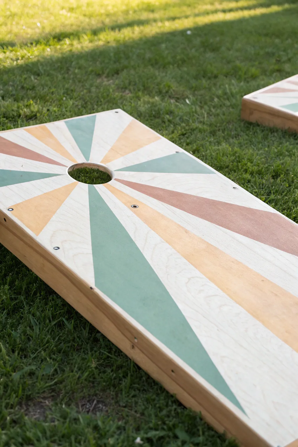 Sunburst rays radiating from the hole for a modern boho cornhole board paint idea.
