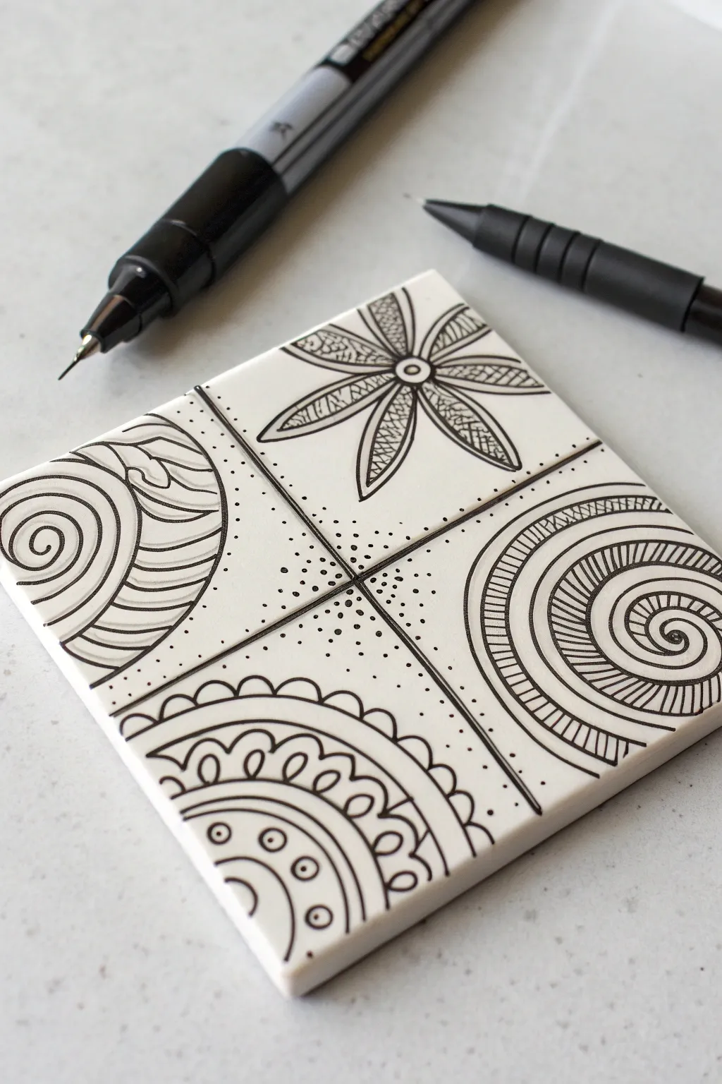 Zentangle-inspired tile doodles in crisp black ink, with a fineliner paused mid-stroke.